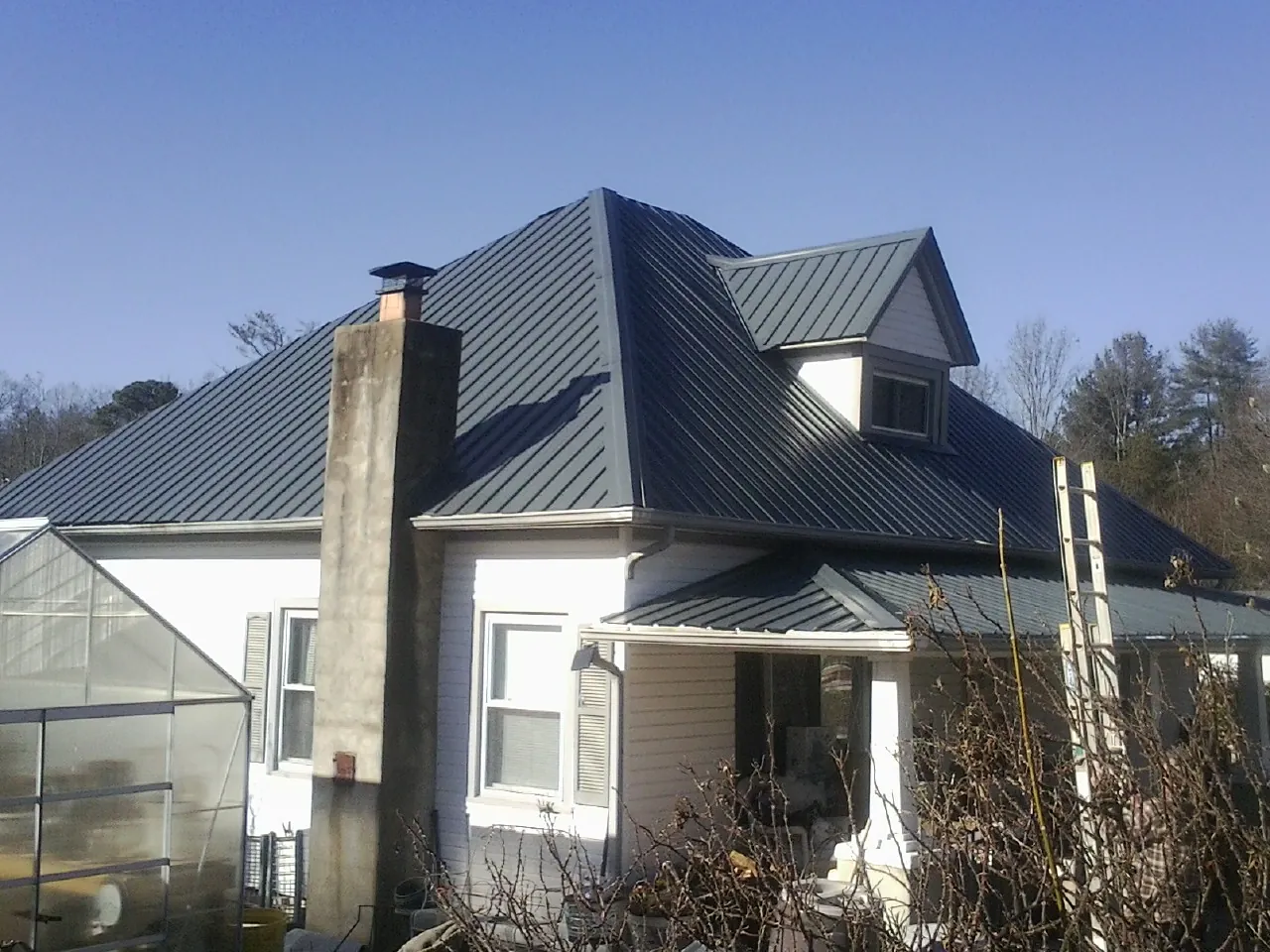 Dark blue standing seam metal roof on a white farmhouse with dormer — Slate & Tile Roof Repair by Roofing Brothers in New England