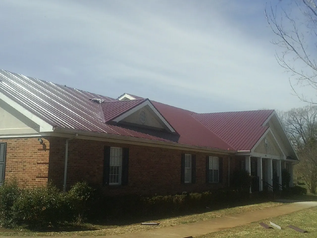 Red metal roof with gabled entries on a long brick building, from a Hail Damage Roof Repair job in New England