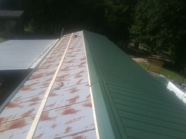 Old rusted panels beside newly installed green metal roofing — Wind Damage Roof Repair by Roofing Brothers in New England