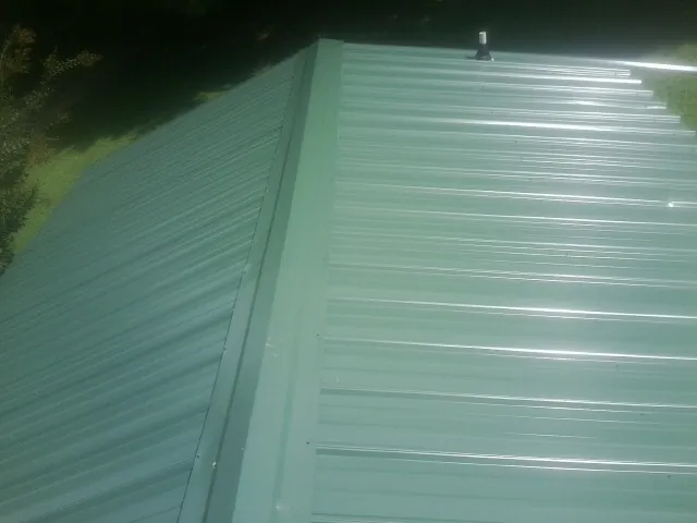 New green metal panels meeting at the ridge of a roof — Flat Roof Repair work by our crew in New England