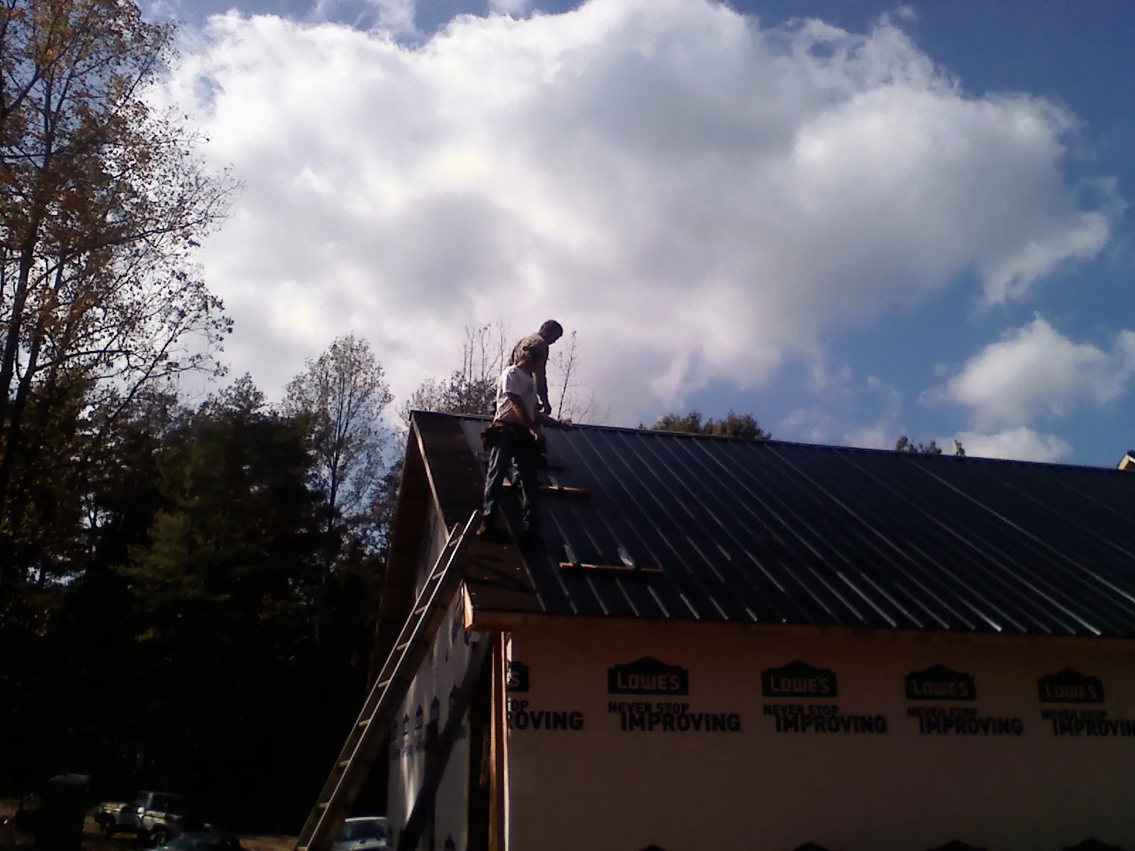 Roofer fastening dark metal panels high against a cloudy sky, from a Roof Inspection job in New England