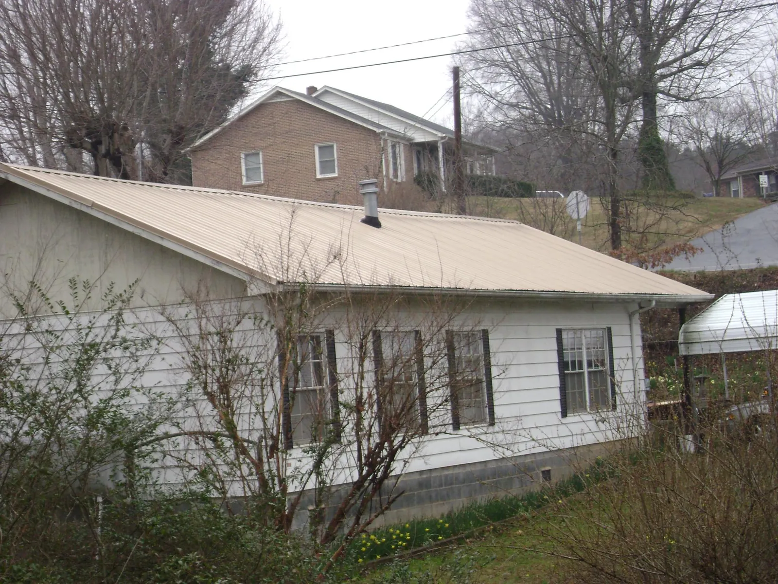 Tan metal roof on a white sided house set into a hillside — Commercial Roofing by Roofing Brothers in New England